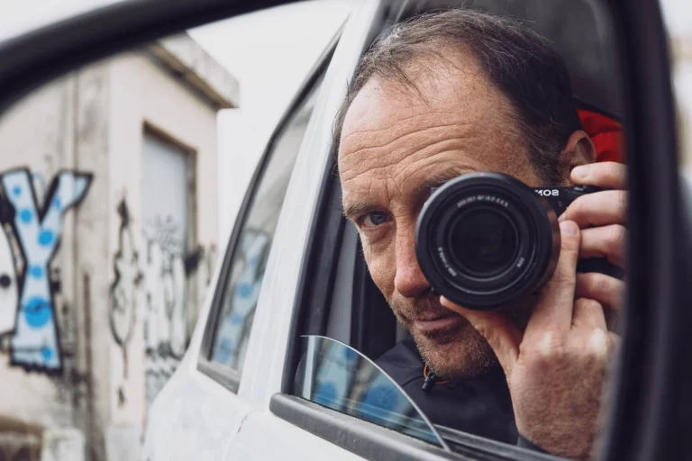 Autoportrait du photographe tenant son appareil photo, vu a travers le retroviseur d'une voiture