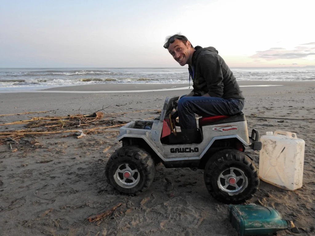Homme souriant assis sur une petite voiture électrique pour enfant, sur la plage